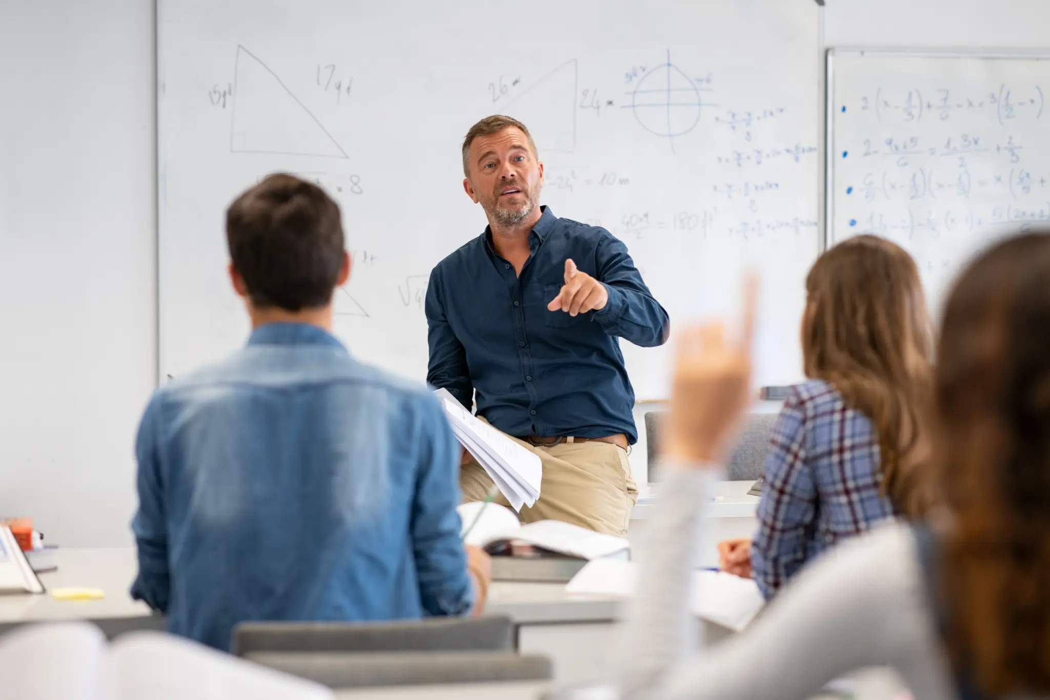 stock-photo-professor-pointing-at-college-student-with-hand-raised-in-classroom-student-raising-a-hand-with-a-1836272266
