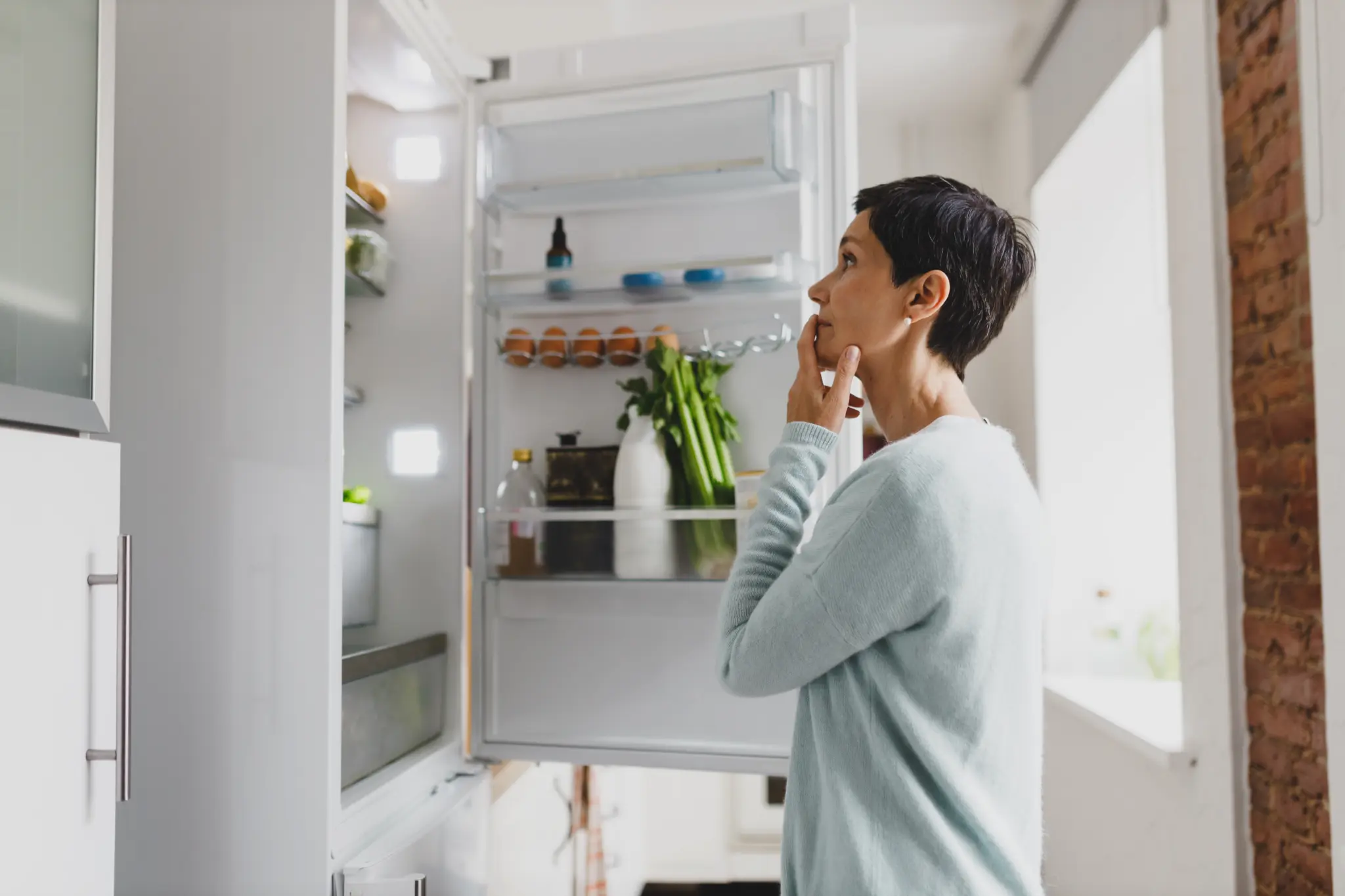 stock-photo-side-view-of-mature-female-with-short-hair-standing-in-front-of-opened-refrigerator-at-home-with-2486003153