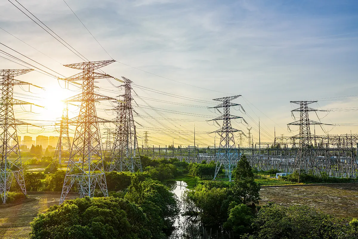 High voltage transmission towers and electrical substation at sunset. Energy grid infrastructure and electricity distribution concept.