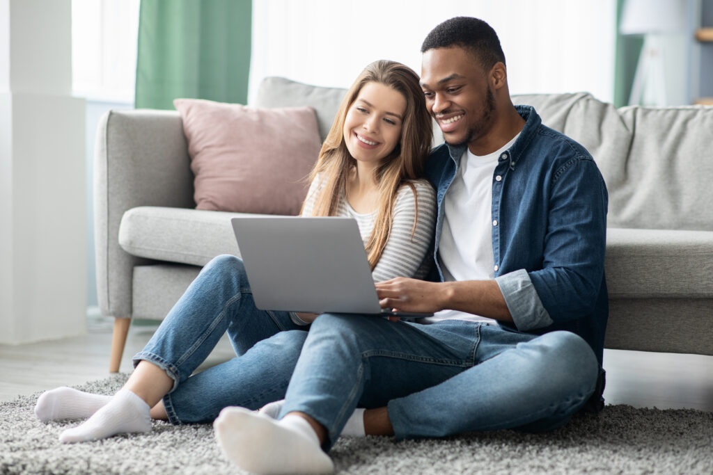 stock-photo-cheerful-millennial-mixed-couple-spending-time-with-laptop-at-home-happy-young-interracial-lovers-1963515223