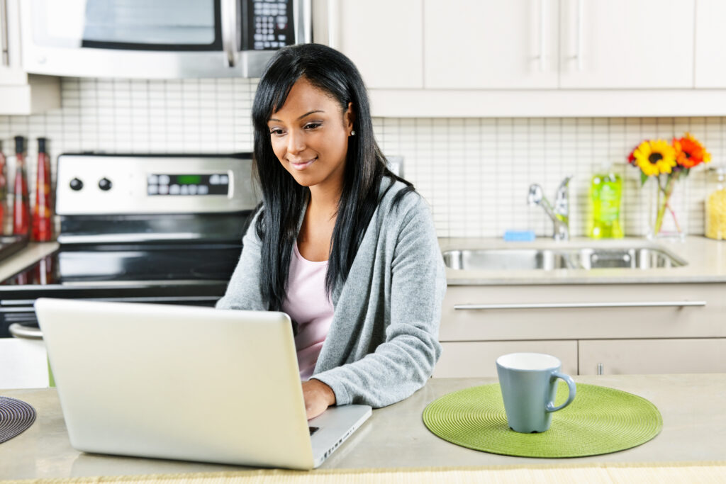 stock-photo-smiling-black-woman-using-computer-in-modern-kitchen-interior-65616760