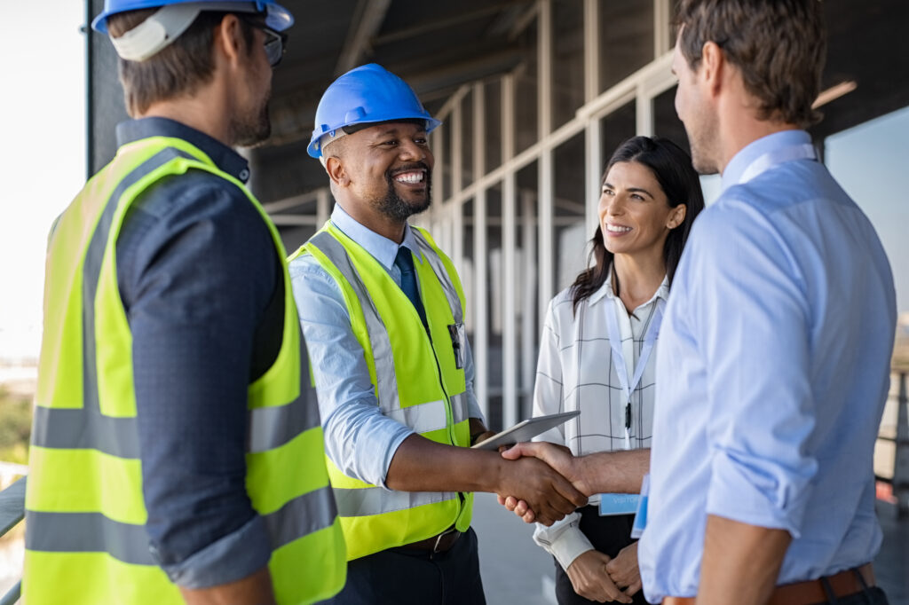 stock-photo-smiling-engineer-shaking-hands-at-construction-site-with-happy-architect-handshake-between-african-1662291403