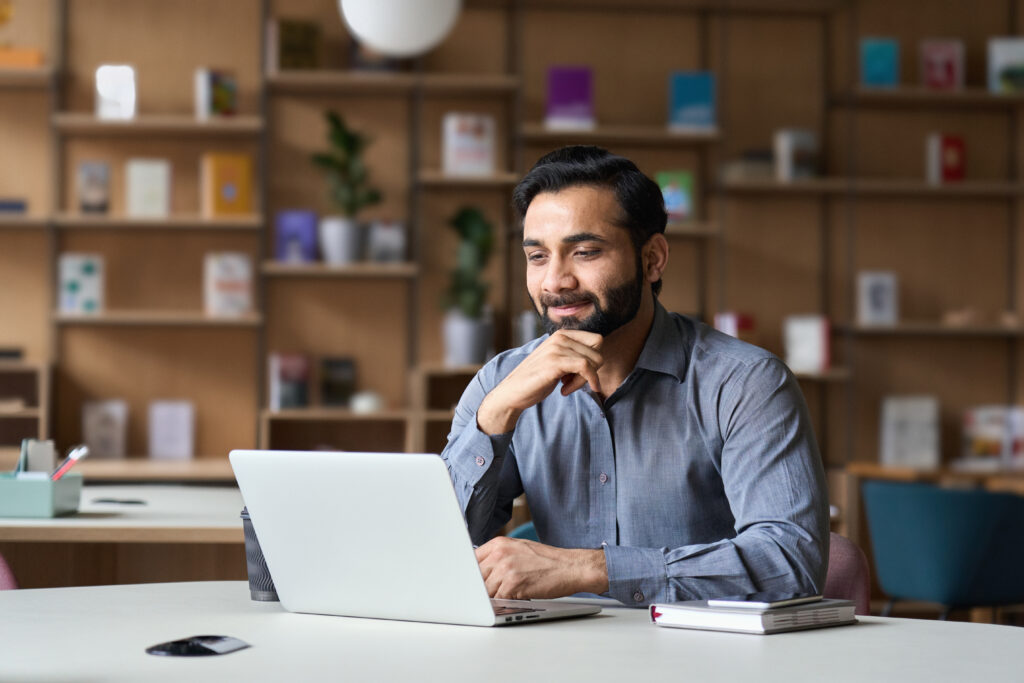stock-photo-smiling-indian-businessman-working-on-laptop-in-modern-office-lobby-space-young-indian-student-1935739078