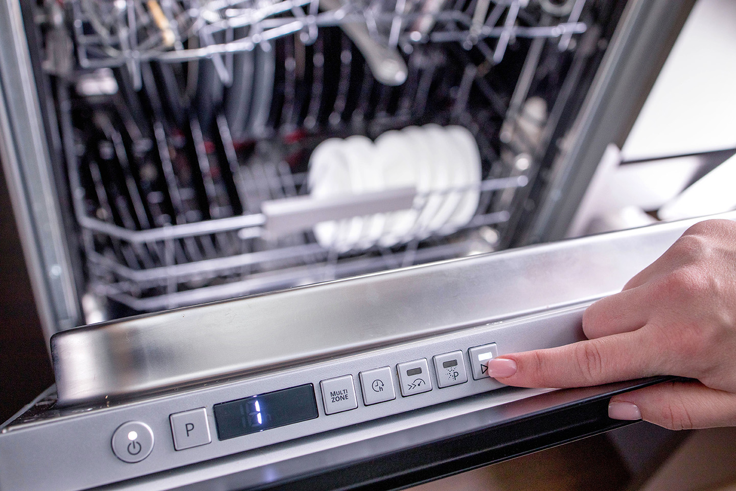 Woman's hand turns on the dishwasher to wash the dishes. Built-in appliances in the kitchen